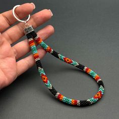 a hand holding a multicolored beaded necklace with a silver ring on it