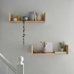 two wooden shelves with plants and vases on them next to a stair case in a white room