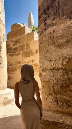 a woman in a long dress standing next to some stone pillars and looking up at the sky