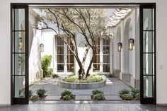 an open door leading to a courtyard with trees and bushes in it, surrounded by windows