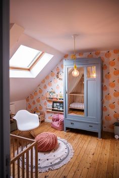 an attic bedroom with orange wallpaper and white furniture, including a blue armoire