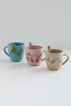 three ceramic cups with designs on them sitting side by side in front of a white background