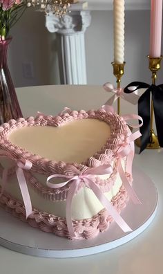 a cake with pink icing and ribbons on a white table next to two candles