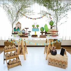 a table topped with cakes and cupcakes on top of wooden crates next to trees