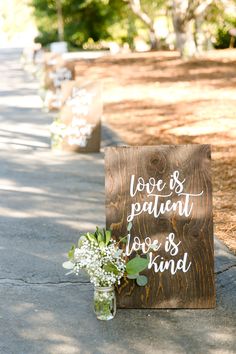 a wooden sign that says love is patient, love is kind next to a vase with flowers