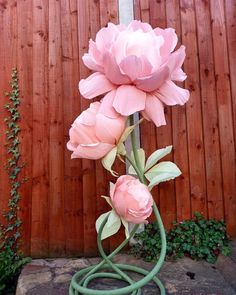 a large pink flower sitting on top of a green hose next to a wooden fence