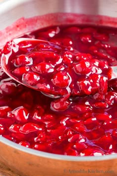 a spoon full of cranberry sauce sitting in a pot on a wooden table