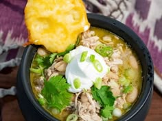 a close up of a bowl of soup with sour cream and cilantro on the side