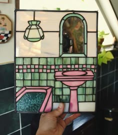 a hand holding up a stained glass window with a sink and mirror in the background