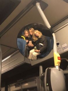 three women sitting on a bus looking in the mirror