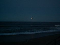 the moon is setting over the ocean with waves