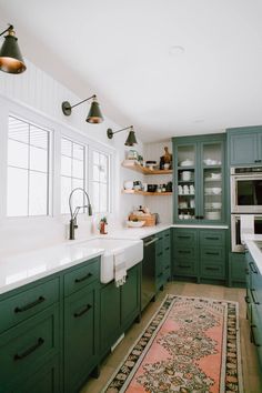 a large kitchen with green cabinets and white counter tops, along with a rug on the floor