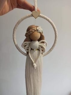 a hand holding a white and brown doll hanging from a rope with a heart on it