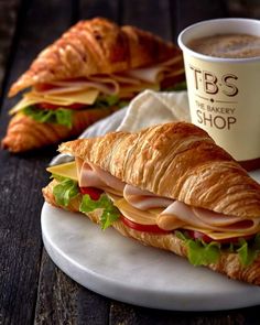 a croissant sandwich on a plate next to a cup of coffee