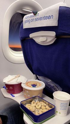 an airplane seat with food on the tray and drinks in cups next to it,