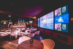 tables and chairs in a restaurant with large screens on the wall