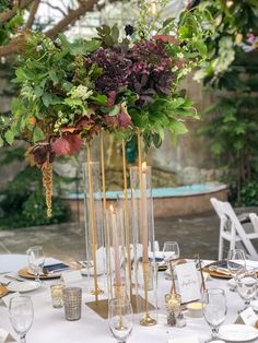 a tall vase filled with flowers and greenery on top of a white table cloth