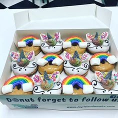 a box filled with lots of cupcakes covered in frosting and rainbow toppings