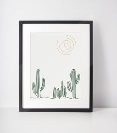 a black frame holds a drawing of cactuses