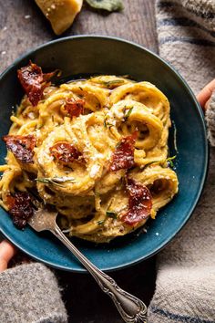 a bowl filled with pasta and bacon on top of a blue plate next to two forks