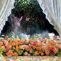 an elaborate display with flowers and butterflies in the air, surrounded by white drapes