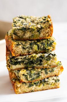 four pieces of bread with spinach and cheese on top are stacked on a white plate