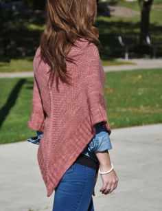 a woman is walking down the sidewalk with her hand in her pocket and wearing a pink sweater