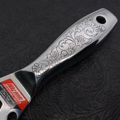 a silver and black knife with ornate designs on it's blade, resting on a black surface