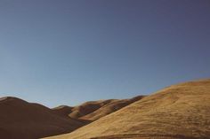 the sky is clear and blue over some hills in the desert, with sparse grass on each side