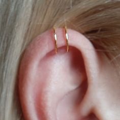 a woman's ear with two small gold hoop earrings