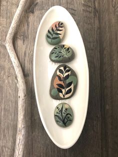 three painted rocks sitting on top of a white plate next to a twig branch