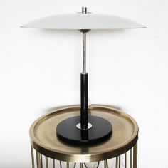 a table lamp sitting on top of a metal stand with a black base and white lampshade