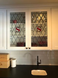 a kitchen with white cabinets and black counter tops, two glass windows above the sink