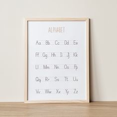 a white framed alphabet print on a wooden shelf next to a wall with a wood frame