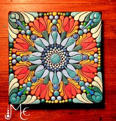 a colorful tile on a wooden surface that looks like it has been painted with acrylic paint