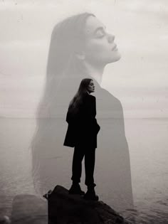 a woman standing on top of a rock next to the ocean with her hair blowing in the wind