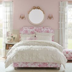 a bedroom with pink walls and white bedding in front of a round mirror on the wall