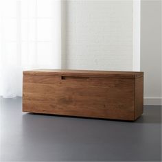 a large wooden box sitting on top of a floor next to a window with white curtains