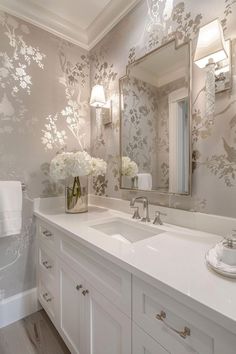 a bathroom with floral wallpaper and white vanity tops, along with a large mirror above the sink