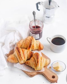 three croissants on a cutting board with butter and jam in the background