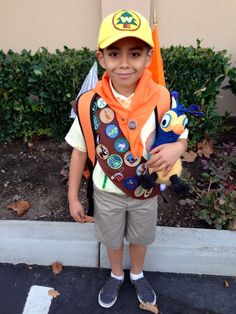 a young boy wearing an orange and brown hat holding a stuffed animal in his arms