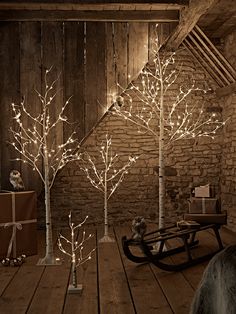 lighted trees in the corner of a room with a sleigh on the floor