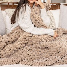 a woman is sitting on a couch wrapped in a blanket and smiling at the camera