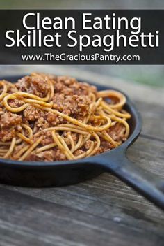 a skillet with spaghetti and meat in it sitting on a wooden table next to a bottle