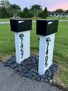 two black and white mail boxes sitting on top of a pile of rocks in the grass