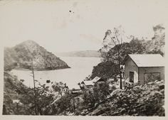 an old black and white photo of some houses by the water with mountains in the background