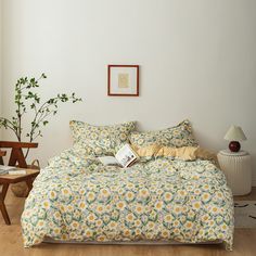 a bed with yellow and green flowers on it in a room next to a plant