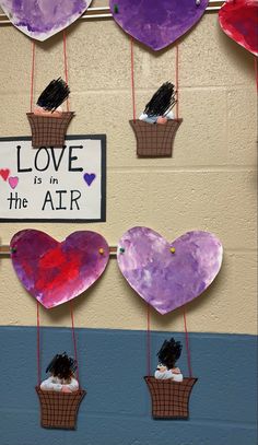 some paper hearts are hanging from strings on a wall with a sign that says love is in the air