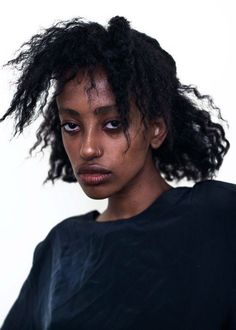 a close up of a person wearing a black shirt with curly hair and blue eyes