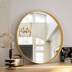 a round mirror sitting on top of a wooden table next to a vase with flowers